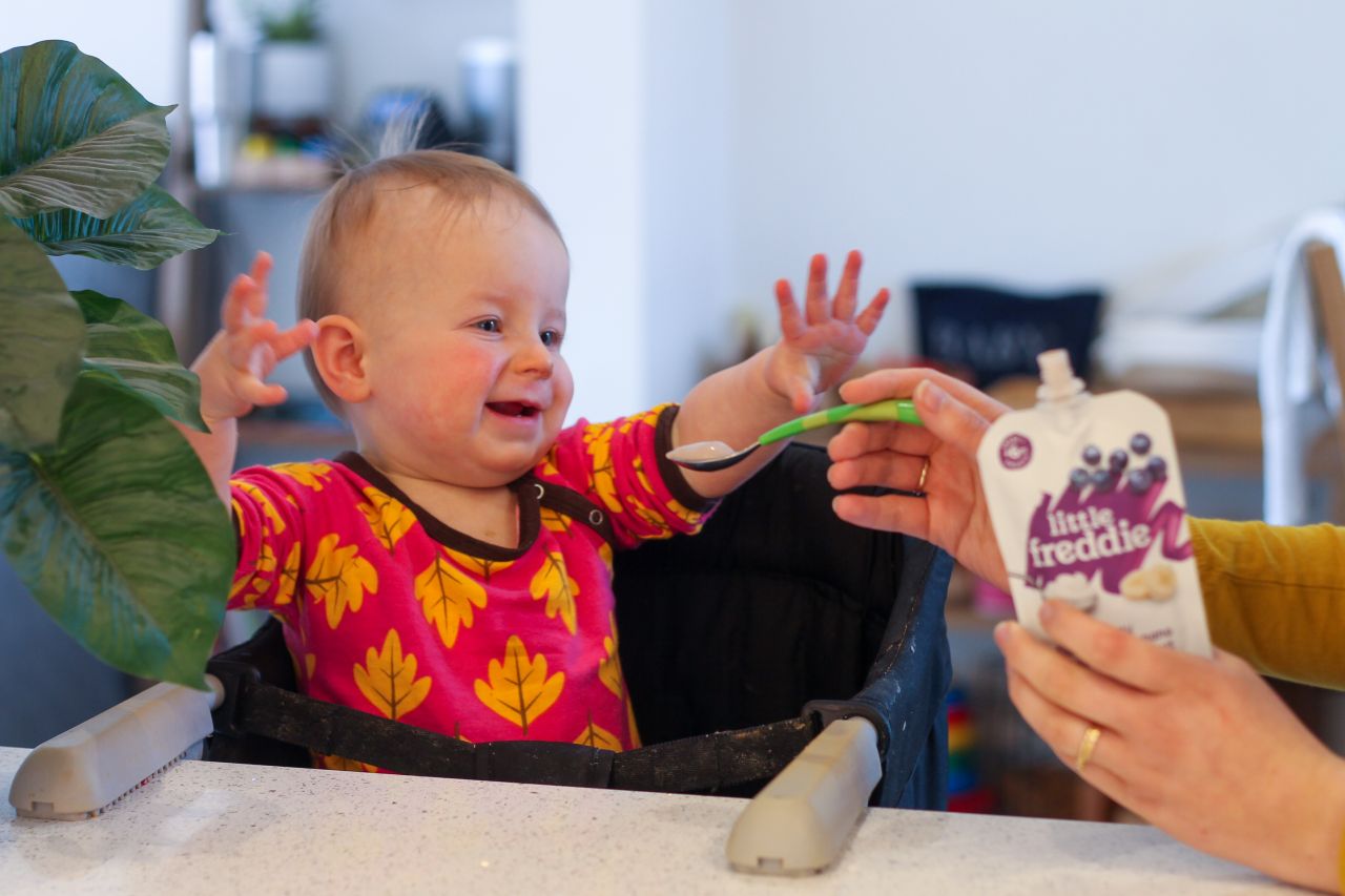 1 year old eating Little Freddie creamy blueberry & banana yoghurt pouch from a spoon